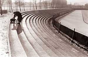 Black and white photograph of a man and his dog who are playing on the concrete terraces of the Ljudski vrt stadium.