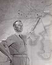 Black and white photo of a middle-aged man wearing military uniform pointing a stick at a map of the Tokyo region of Japan