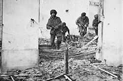 Four men in bombed building walking over rubble