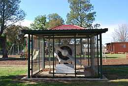 An aircraft engine and propeller sits under fenced, roofed shelter in a park