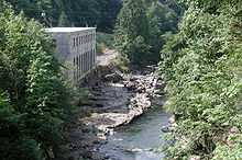 A small river flows by a two-story masonry building with many windows.