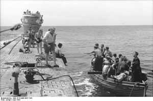 A black-and-white photo showing a submarine parallel to a row boat.