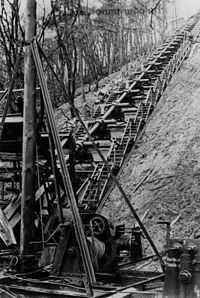 A single Hochdruckpumpe barrel mounted on the side of a steep wooded hill, with flights of steps on each side of it and machinery in the foreground