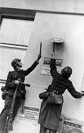 Photo of two German soldiers removing Polish government insignia from a wall.