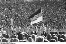 People march behind a large flag surrounded by spectators