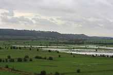 Water on grassy lowland with hills in the distance.