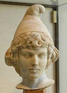 A marble bust of a curly-haired boy wearing an edgeless conical cap with the rounded peak bending forward