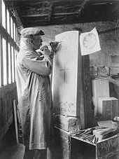 a man carving the a maple leaf onto a gravestone, in a workshop, with a hammer and chisel.