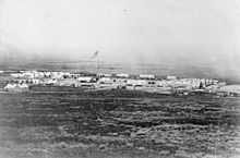 Historic photograph of Camp Douglas, a collection of tents and a few buildings around a tall U.S. flag amidst a desolate flat, which later became Fort Douglas.