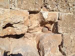 A weathered stone wall with a section broken away in the centre. Two cannonballs are partly visible, deeply embedded in the broken section of the wall.