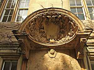 A large decorated shell-like stone canopy, with a shield in the centre and carved foliage around; a cherub's head underneath the hood