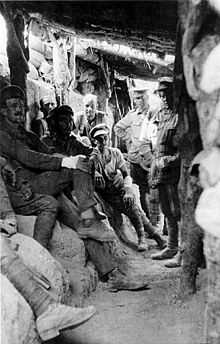Soldiers sitting in a trench beneath a log roof