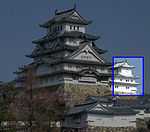 A small three-storied castle tower next to a large five-storied tower. Both have white walls, dark roofs and are built on a platform of unhewn stones.