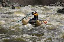 A man on a cataraft paddling through rapids of foam and green water