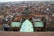 Looking down on a cruciform green-copper roof, with a tower at the centre, in the middle of a city