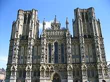 Large ornate grey stone facade of a building. Symmetrical ith towers either side.