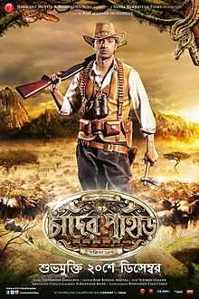 An young man with Indian origin is looking back with a rifle on his shoulder, having a backdrop of jungle, animals, mountain ranges and the logo art of the film