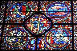 Part of a large window. It is divided into four circular panels with a quatrefoil (or four-lobed section) between them and an arched segment beneath. To the lower right, a knight, Sagittarius, is being welcomed home. At the centre a man empties a water pot, symbolising Aquarius and a two-faced figure symbolises New Year. To the upper right, are the two fish of Pisces. The other sections show each month's activities: grapevine pruning, bell-ringing and sitting by the fire.