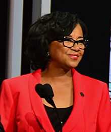 A woman in a red blazer smiles in front of a microphone.