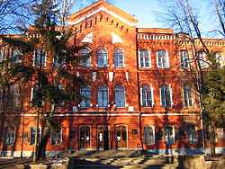 Brown, three-story building with arched windows and trees in front