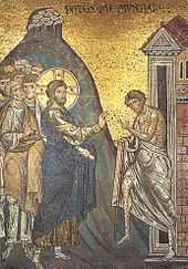 Jesus, his head surrounded by a halo, puts his hands on a leper, thereby healing him.