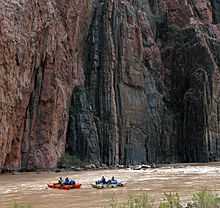 View of two small boats in a river, with high cliffs rising immediately behind them