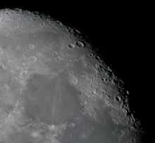 A black-and-white image of Earth's Moon. A distinct shadow has fallen over the upper-right portion of the Moon, visibly separating its light and dark sides. Photography by Bresson Thomas.