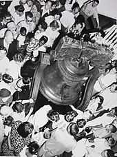 number of tourists, of all races and ages, dressed in the fashions of sixty years ago, gather around the Liberty Bell.