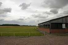 View of green, very flat field with a single story building to the right