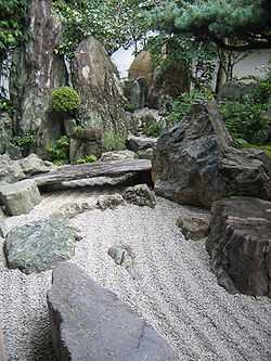 Rock garden with raked gravel and large stones including one placed like a bridge.