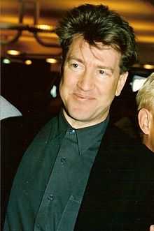 A man in a green shirt and a black suit smiles at the camera.