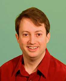 David Mitchell wearing a red shirt looks at the camera