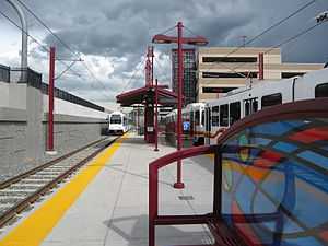 Station platform and canopy with a white tram present and multiple buildings visible at rear.