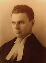 Diefenbaker with an intense look in his eyes. Still a young man, he wears ceremonial robes in this portrait shot; the bands of the robes are visible.