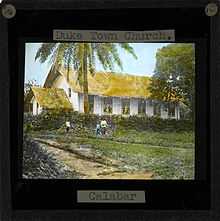 Image of the Duketown Church, Calabar (located within later day Nigeria). Three people stand in front of the white sided church with a thatched roof.; Duketown lies on the Calabar river 50 miles from the coast.
