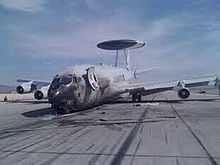 Jet aircraft resting on ramp with a nose-down attitude. The nose was blackened during a fire. On top of it is a circular radar.