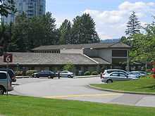 A small building surrounded by trees, with a parking lot in front of it.