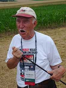 Man in a ball camp and white Tshirt holding a thin rod and standing in a field