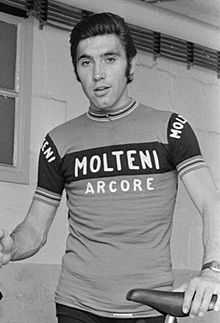 Merckx holding a bicycle. His shirt says "Molteni Arcore", and his hair is slicked back.