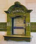 An elaborate ticket office window, tiled in green terracotta, with the word "TICKETS" above the window and "OUT" and "IN" on the left and right sides