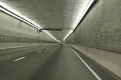 A two lane freeway without any safety lanes or shoulders is proceeding down a lighted square passageway.