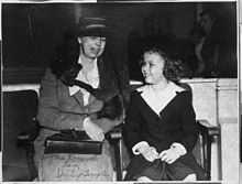 Photograph of Eleanor Roosevelt seated with Temple immediately to her left. The two are looking at each other apparently engaged in conversation.