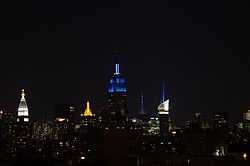 Upper floors of the Empire State Building lit in blue, amid other lit skyscrapers