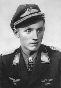 A black and white photograph of a smiling young man wearing a military uniform, peaked cap, various military decorations including a neck order in shape of an Iron Cross.