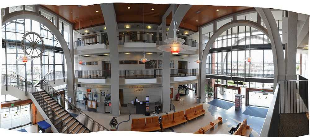 The lobby of a large building, with balconies from two upper stories framed by large steel arches.