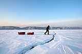 A man pulling two sledges on a frozen lake, approaching a crack in the ice