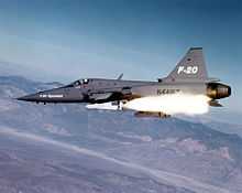 Gray jet fighter aircraft fires a white missile.