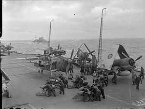 Black and white photographs of several groups of men bent over bombs on the flight deck of an aircraft carrier at sea. Several monoplane aircraft are parked on the flight deck, and another warship is visible on the sea near the carrier.