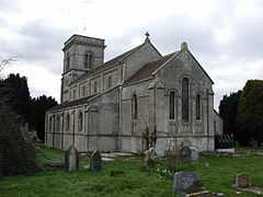 Gray stone building with square tower at far end. Grass and gravestones in the foreground.