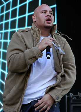 A bald man, wearing a white T-shirt and creamy pants is performing